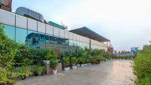 Un edificio moderno con fachada de vidrio, rodeado de macetas con plantas y un patio empedrado.
