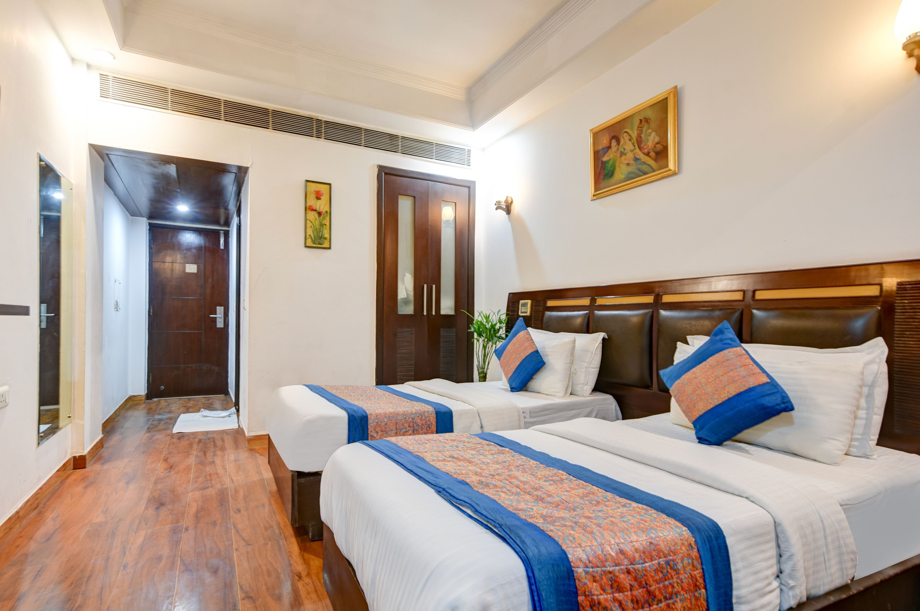 A hotel room with two beds, wooden headboards, and a large painting on the wall.