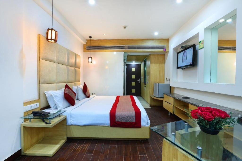 Una moderna camera d'albergo con un letto grande, comodini, una televisione e un tavolino in vetro con fiori.