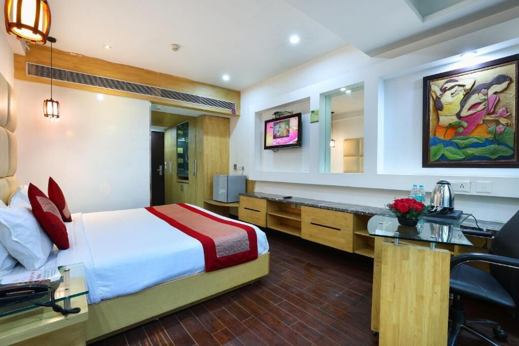 A hotel room with a bed, a desk, a chair, a TV, and a painting on the wall.