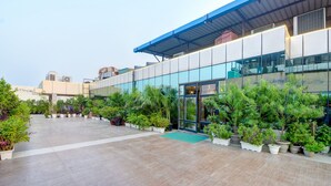 Un edificio moderno con fachada de vidrio, un acceso cubierto y un patio espacioso con plantas en macetas.
