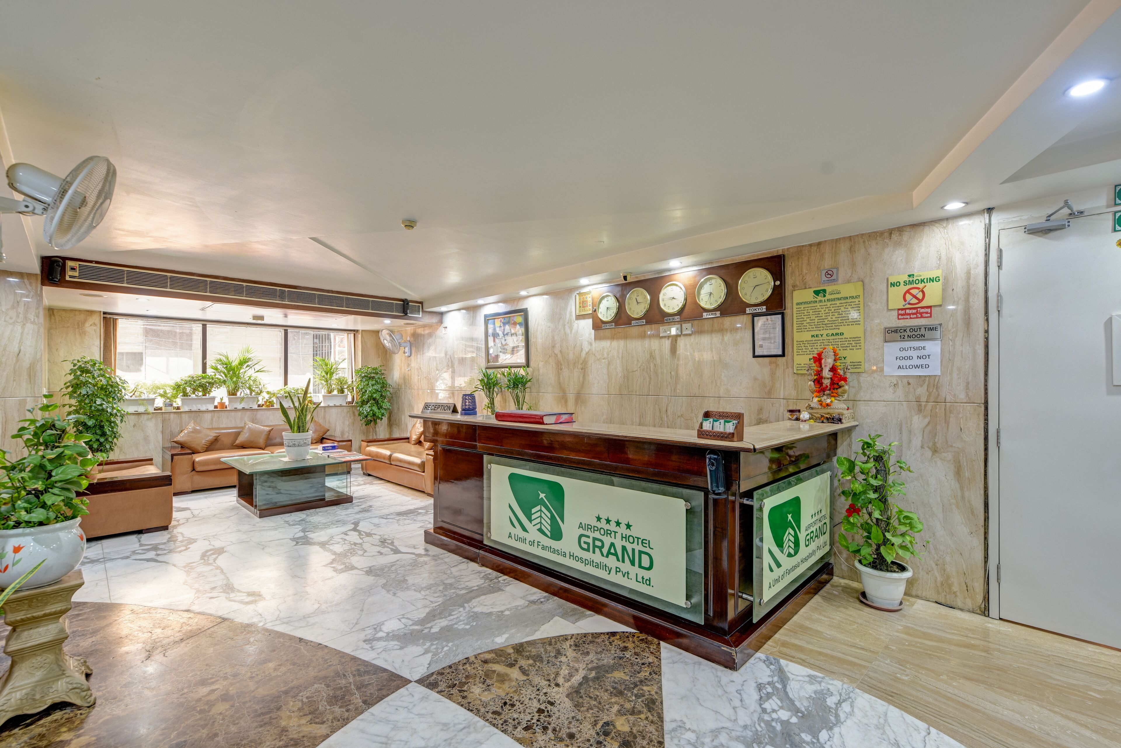 A hotel reception area with a marble floor, a reception desk, a sofa, and potted plants.