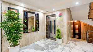 Un vestíbulo con piso de mármol, plantas en macetas, un espejo grande, un ascensor y una escalera.