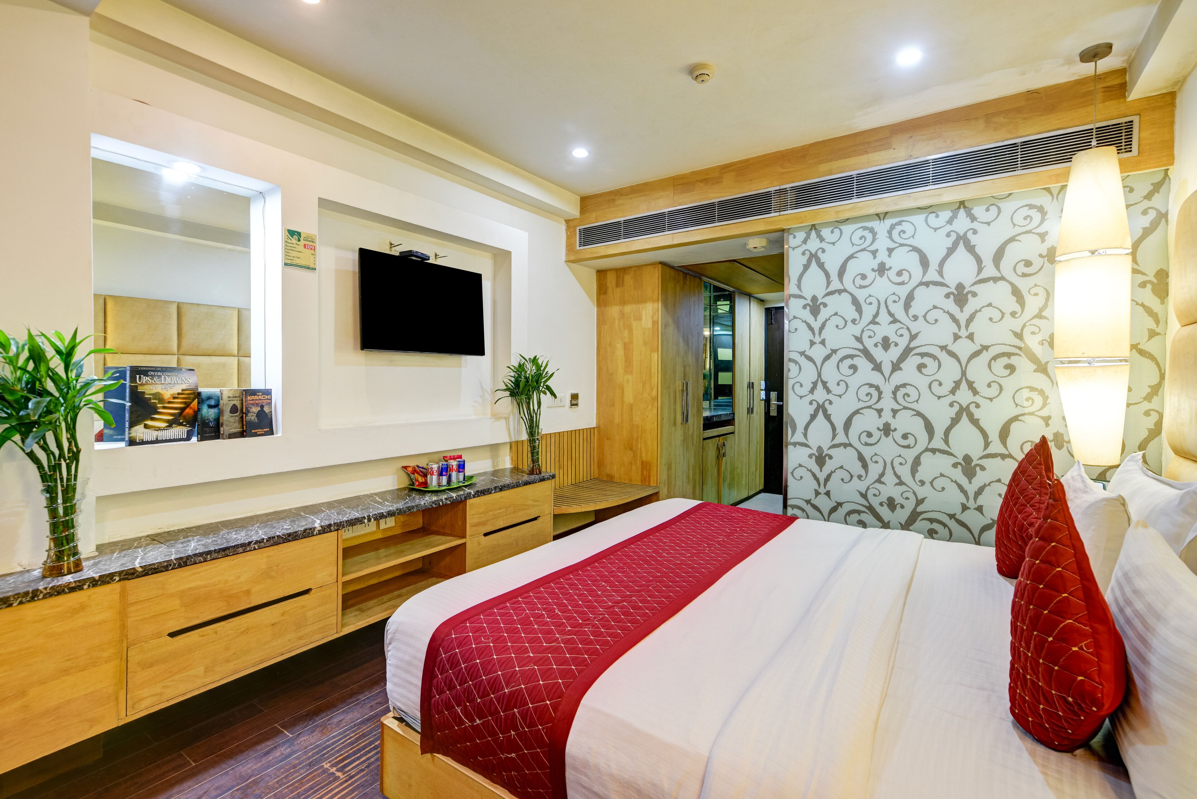 A hotel room with a large bed, a TV mounted on the wall, a wooden vanity, and a mirror.