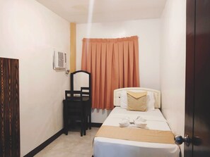 A small, compact hotel room with a single bed, a bedside table, a chair, and a window with curtains. - Amax Inn Cebu (Mandaue)