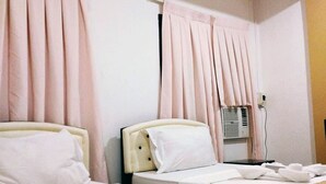 Hotelkamer met twee bedden, elk voorzien van witte lakens en kussens, een nachtkastje en een wandairconditioning.