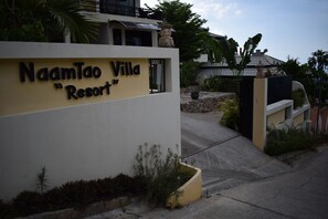 A sign for Naamtao Villa Resort with a modern design, a pathway leading to the entrance, and surrounding greenery.