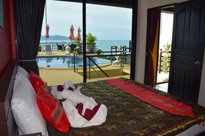 Habitación de hotel con cama, vista a una piscina y al mar, y un balcón con sillas y sombrillas.