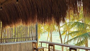 Un área de estar al aire libre con techo de paja, sillas de madera y vista a la playa.