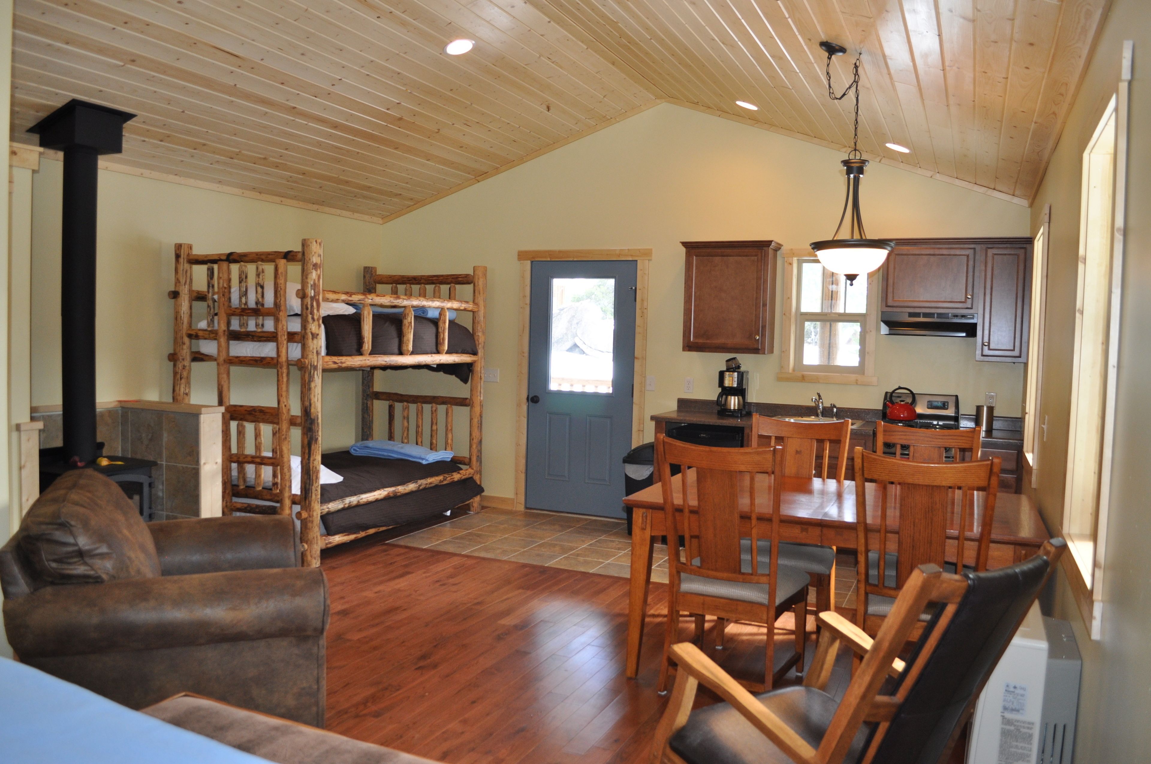 A cozy cabin interior with a dining area, wooden furniture, a bunk bed, and a kitchen.