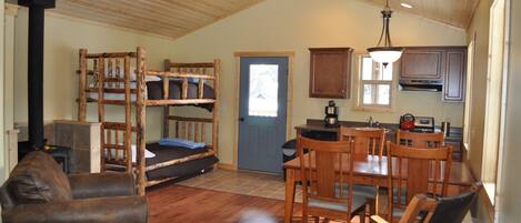 A cozy cabin interior with a dining area, wooden furniture, a bunk bed, and a kitchen.