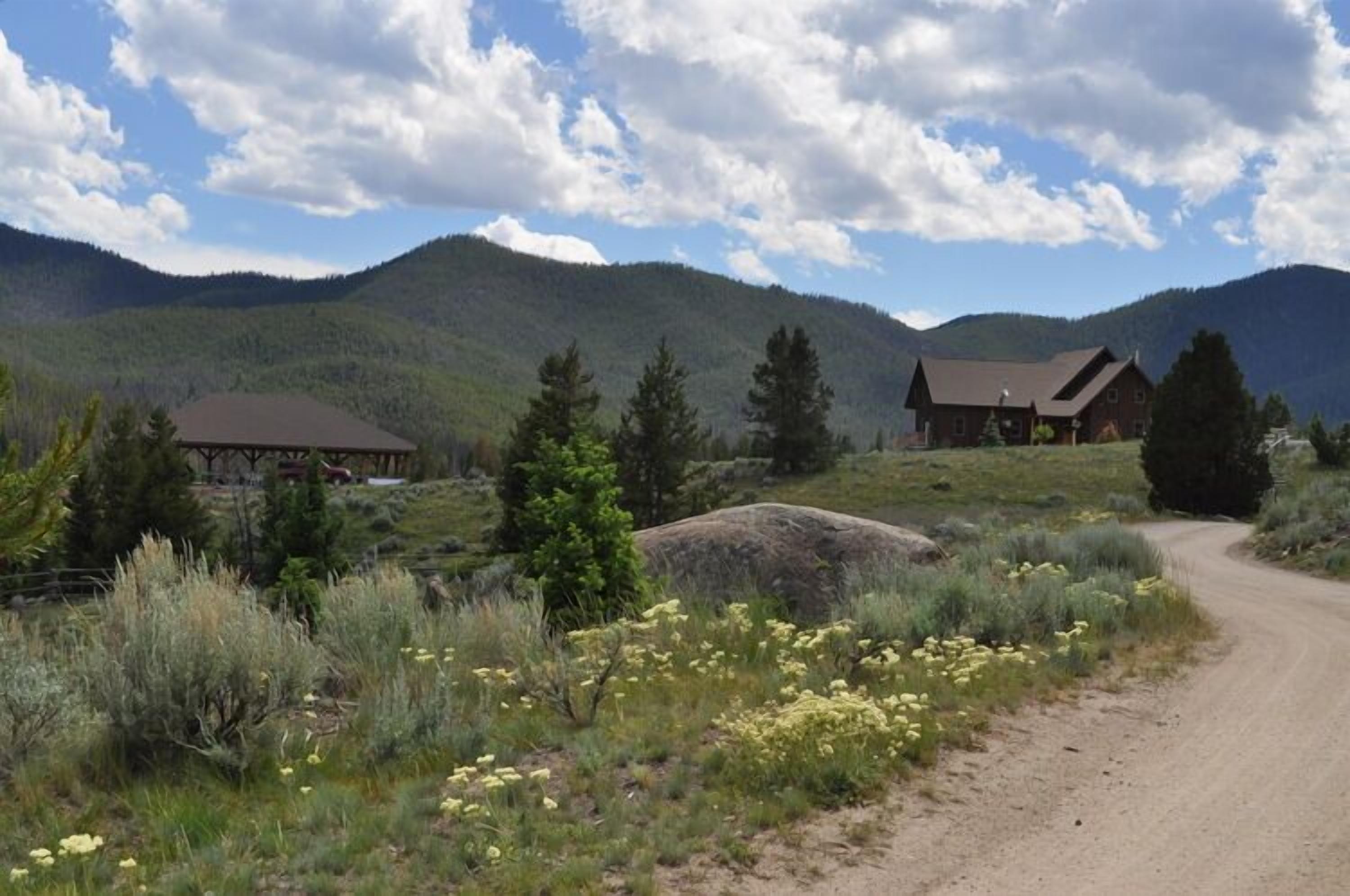 A rural landscape with a dirt road, two wooden cabins, and a mountain backdrop.