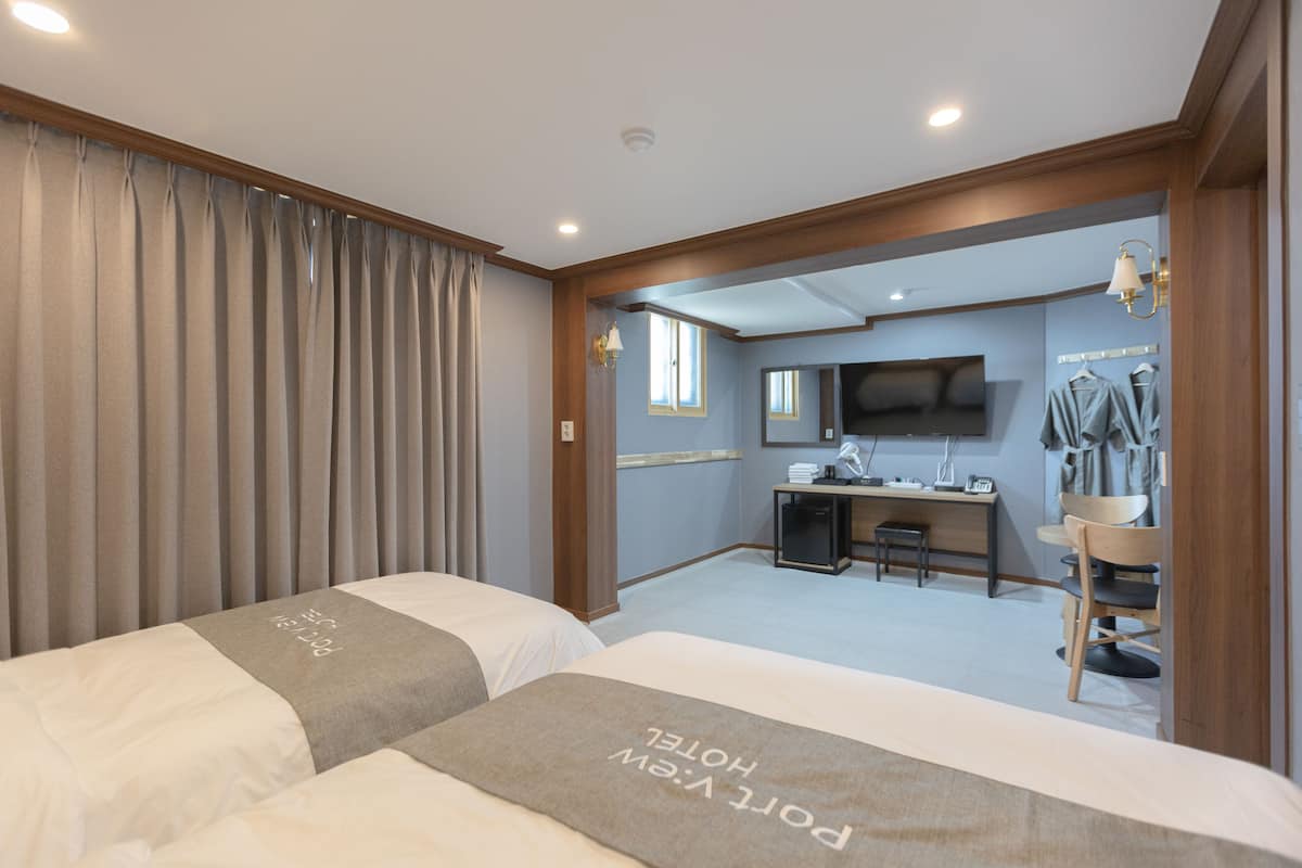 A hotel room with two beds, a desk, a chair, a television, and a mirror.