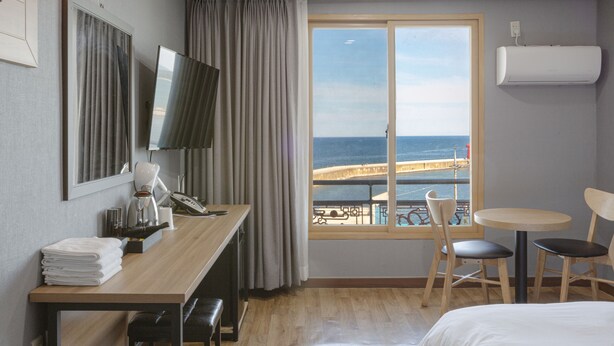 A hotel room with a wooden desk, a bed, a TV, a window with a view of the sea, and a small balcony. - Port View (Yangyang)