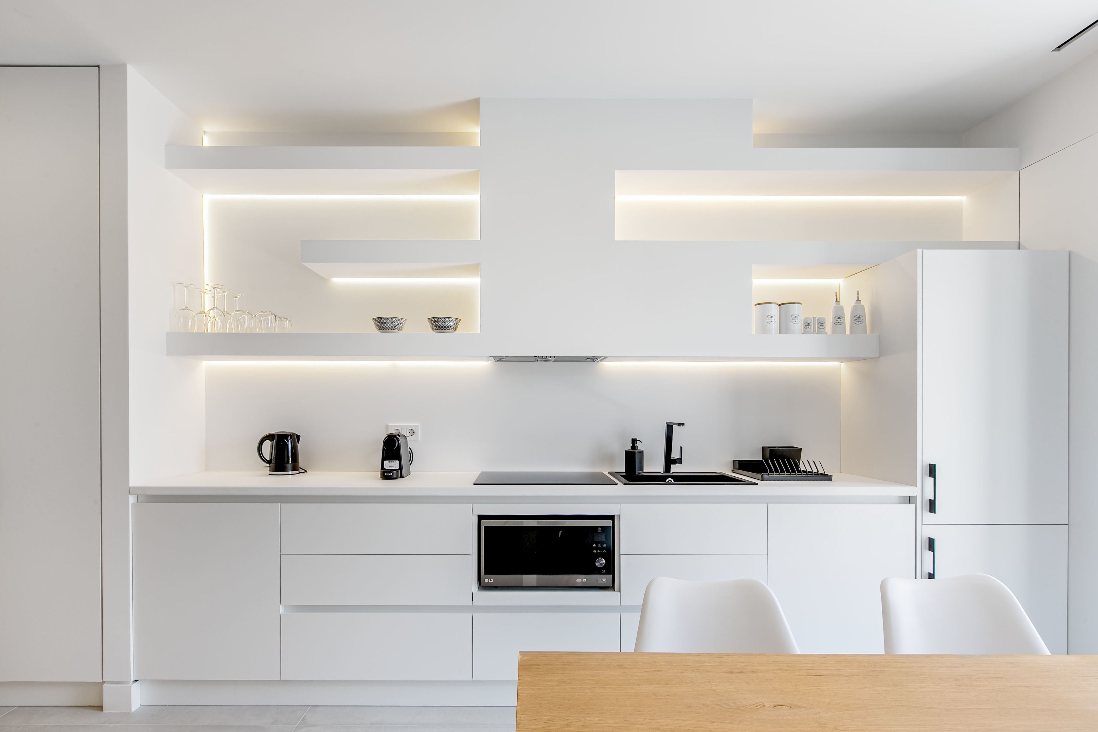 A modern kitchen with white cabinetry, built-in appliances, and under-cabinet lighting.