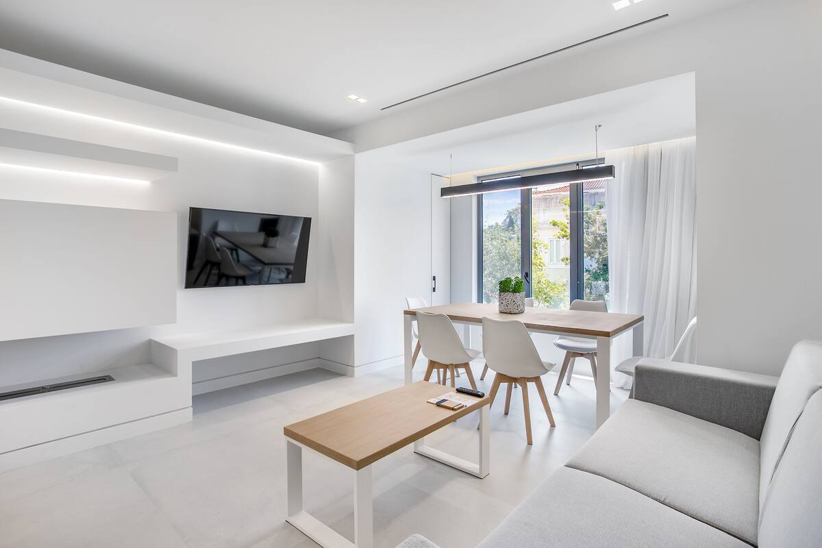 Un salon moderne comprenant un canapé, une table basse, un téléviseur fixé au mur et un coin repas avec des chaises et une table.