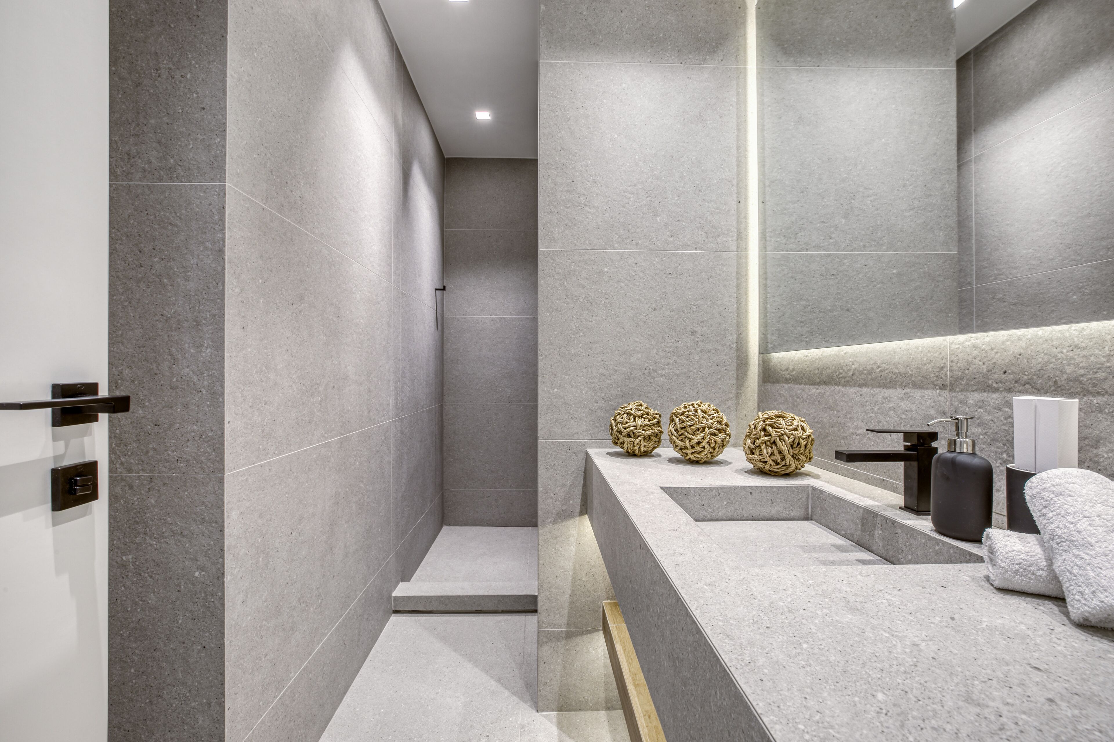 A modern bathroom with grey tiles, a shower area, a vanity with a mirror, and two decorative spheres.