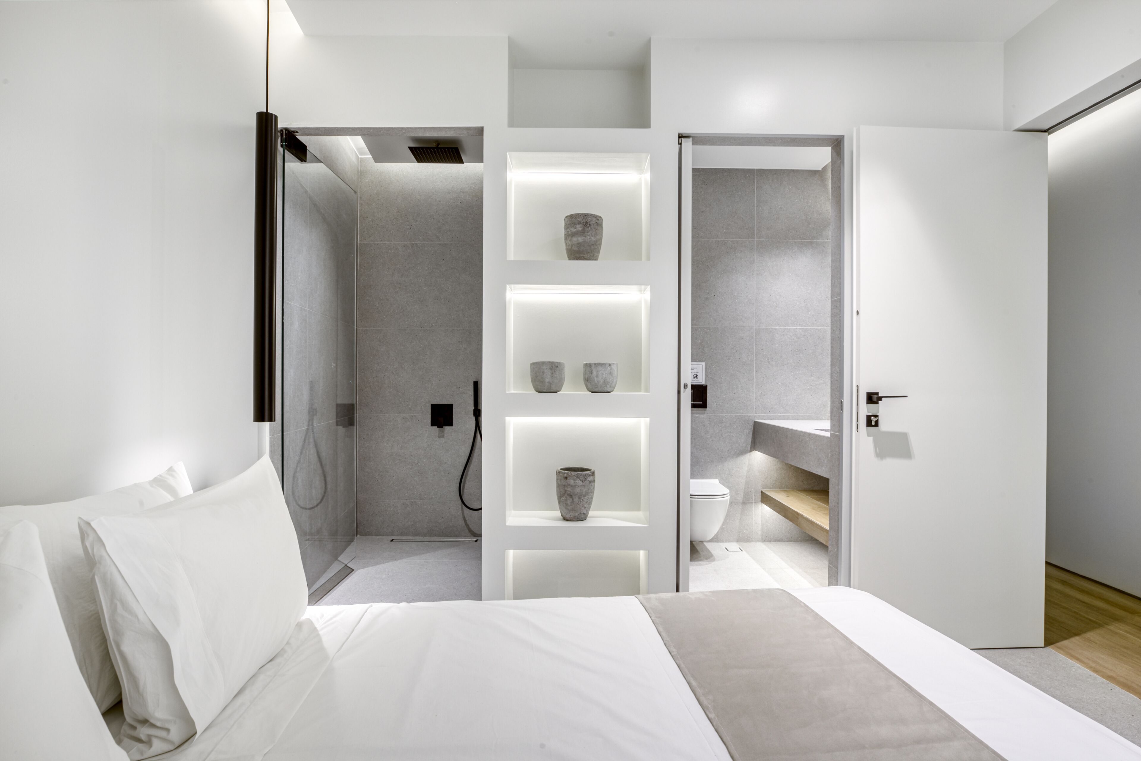 Ein modernes Schlafzimmer mit Bett, Dusche und einem Badezimmer mit Toilette und Regalen.