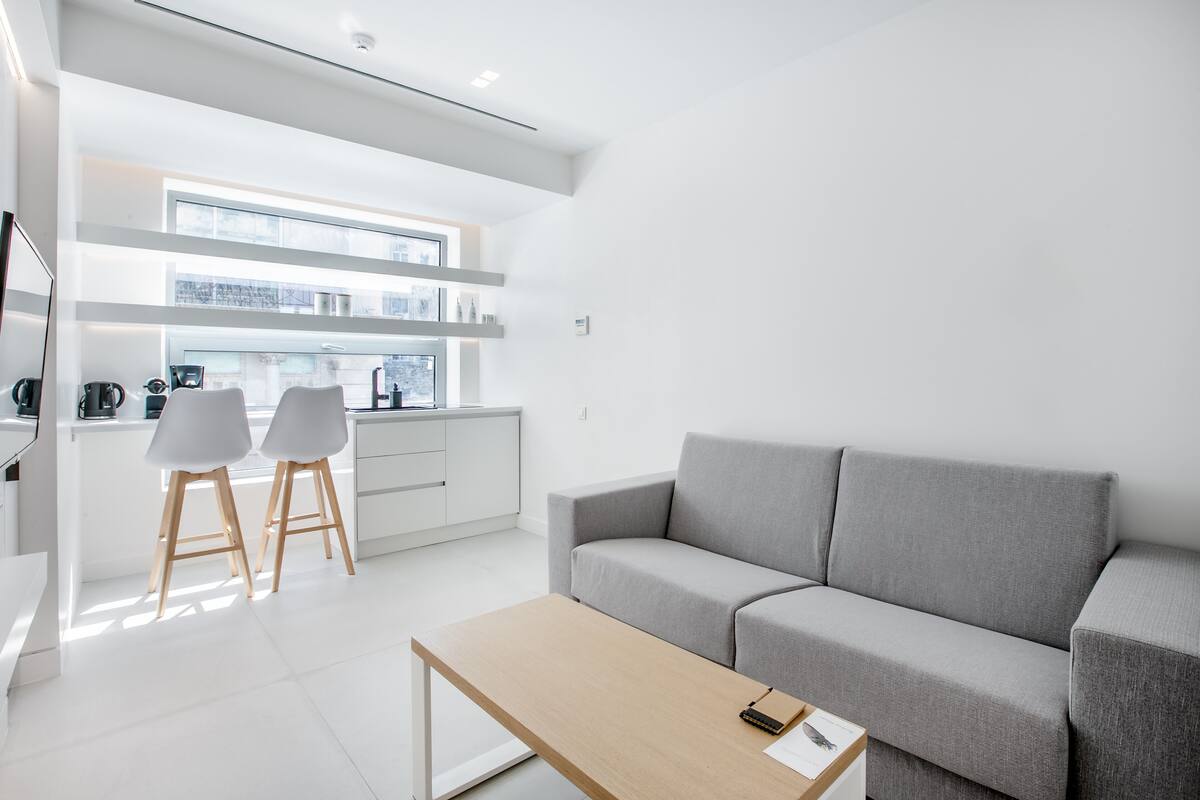 Un salon moderne et minimaliste, avec un canapé gris, une table basse en bois et deux chaises blanches.
