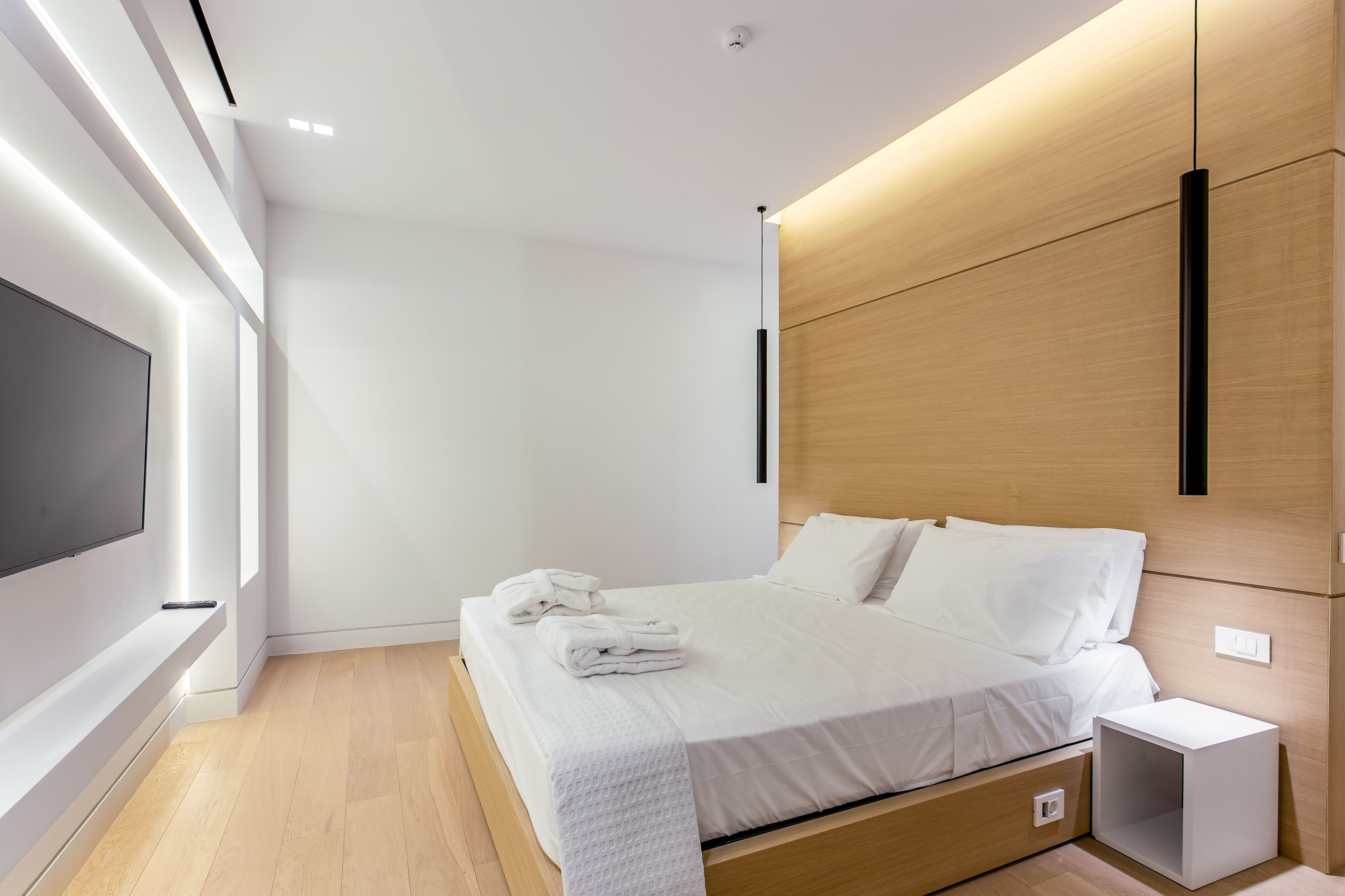 A modern hotel room with a large bed, a TV mounted on the wall, and a wooden headboard.