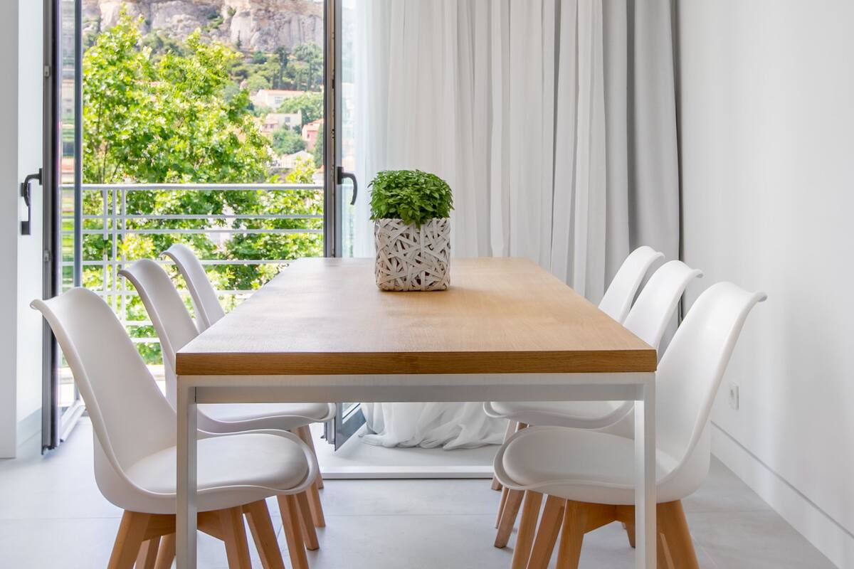Un coin repas avec une table en bois, des chaises blanches et une plante en pot.