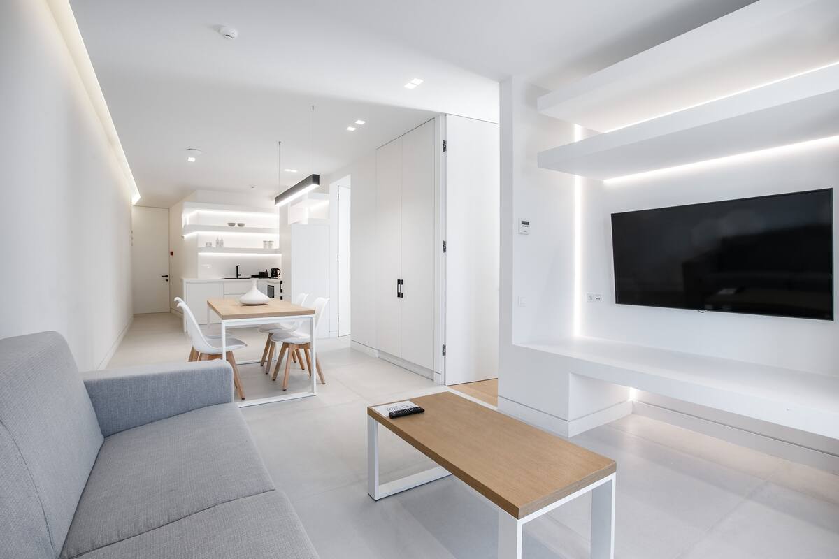 Un salon moderne avec un canapé gris, une table basse en bois et un téléviseur fixé au mur.