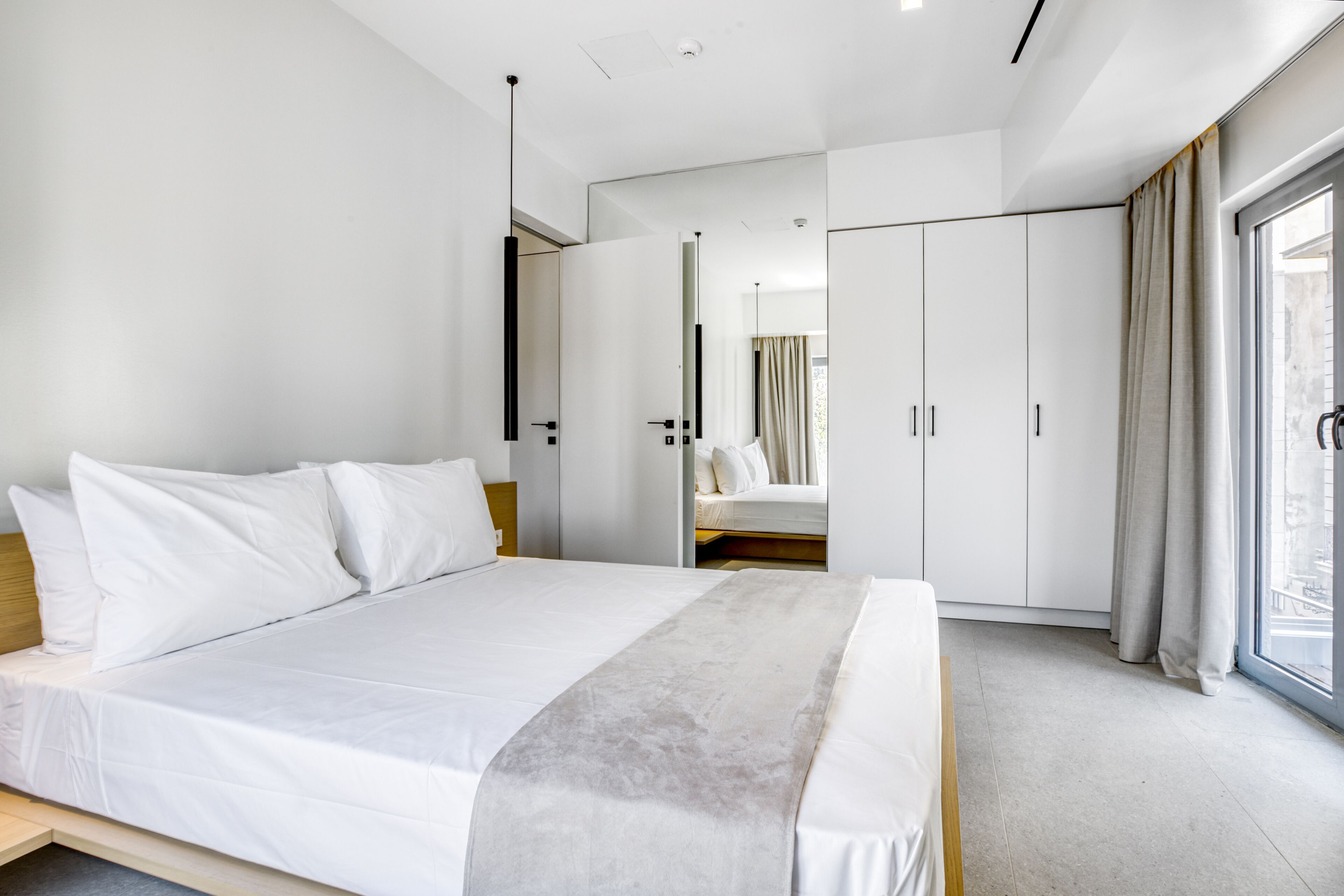 A modern hotel room with a large bed, a wardrobe, and a sliding glass door to the outside.