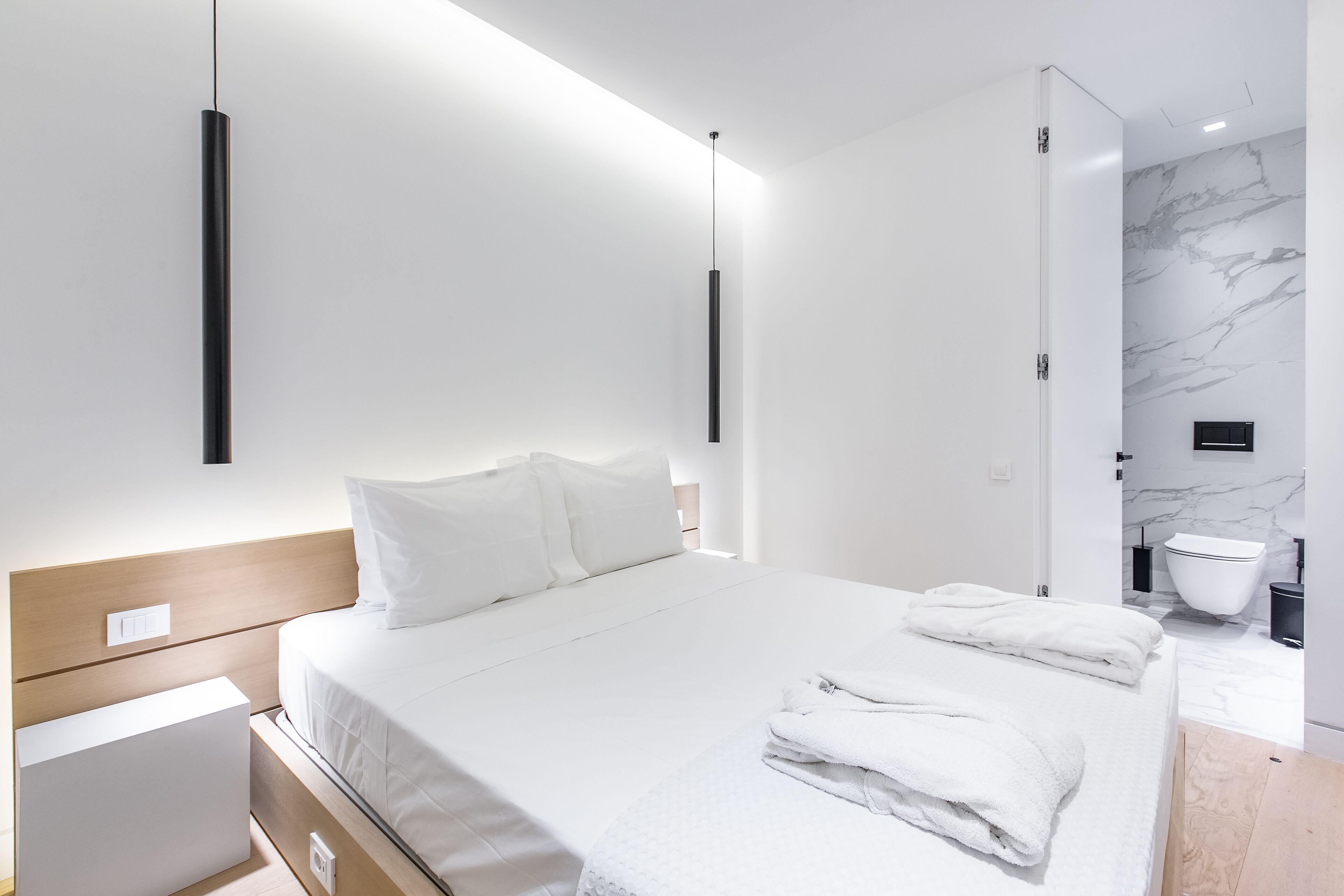 A modern hotel room with a neatly made bed, a bedside table, and a bathroom with a marble wall and a toilet.