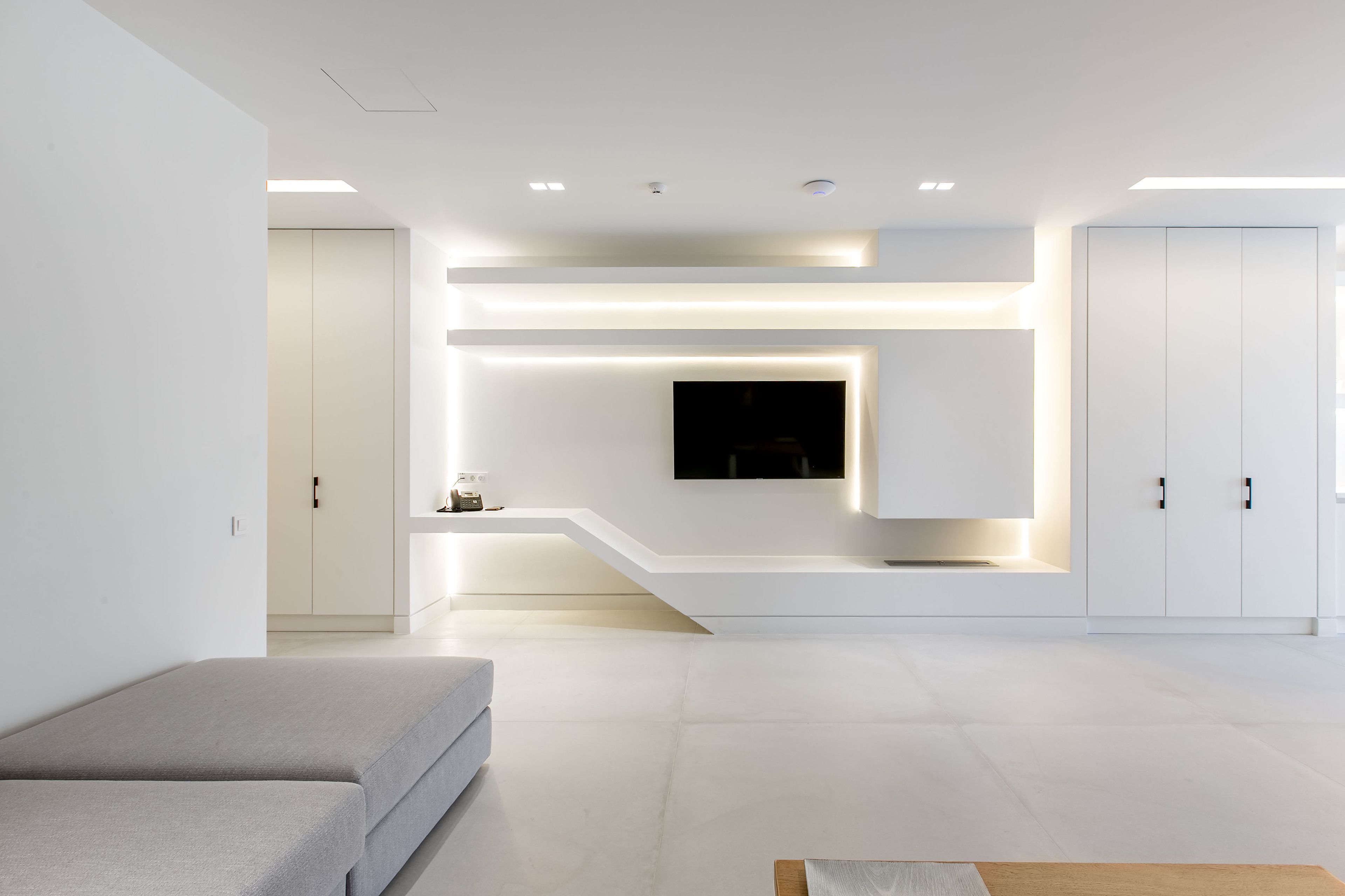 Una sala moderna con televisor de pantalla plana montado en una pared blanca, iluminación empotrada y un banco integrado.