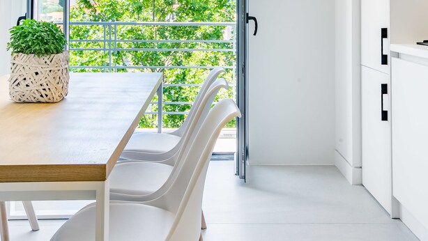 Un interior moderno con comedor, sillas blancas, mesa de madera y vistas a la ciudad y follaje a través de amplias ventanas.