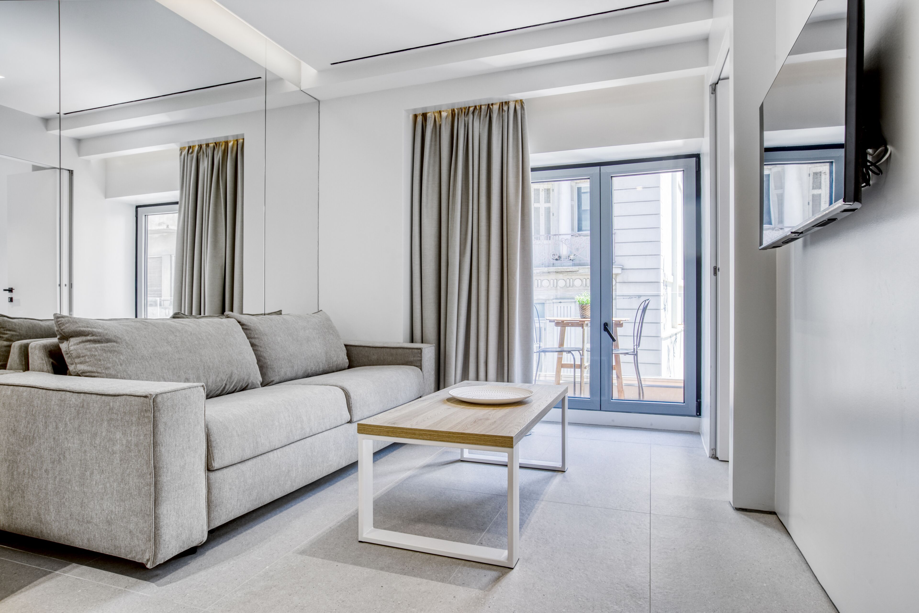 A modern living room with a sofa, a coffee table, and a sliding glass door leading to an outdoor area.