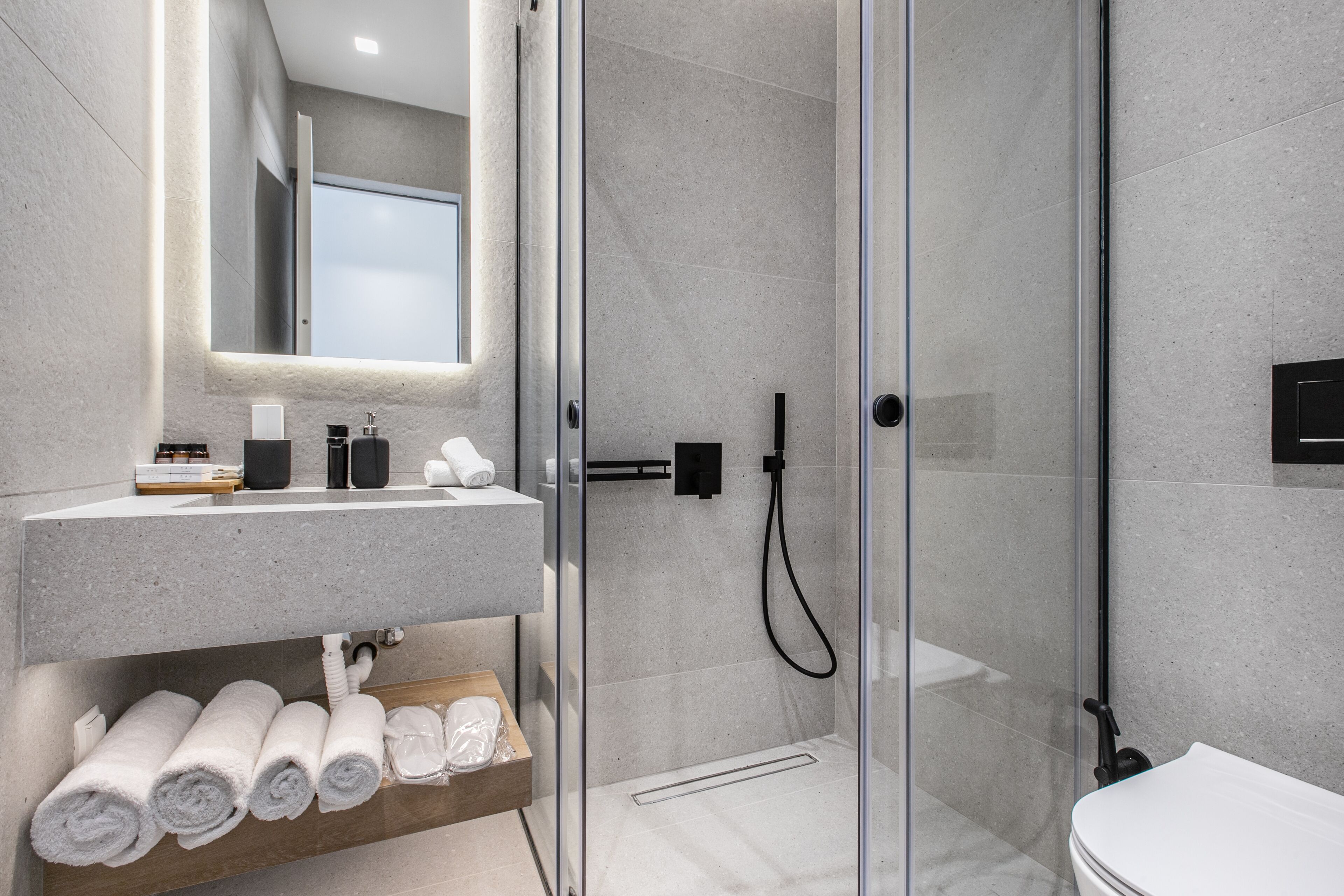 Une salle de bain moderne avec une douche en verre, un lavabo en marbre et des serviettes soigneusement pliées sur une étagère.