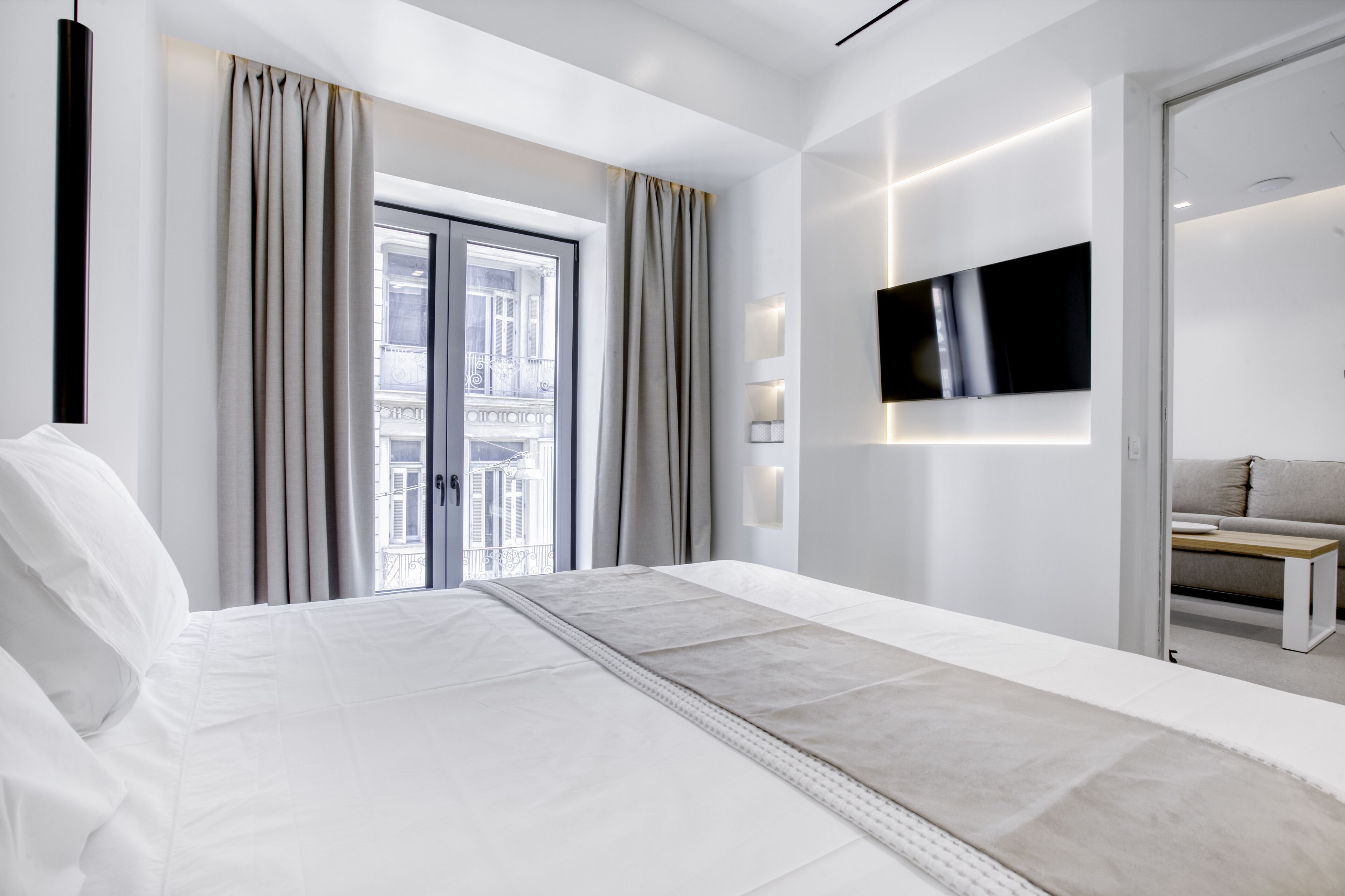 Ein modernes Hotelzimmer mit einem großen Bett, einem an der Wand montierten Fernseher und Blick auf die Stadt durch das Fenster.