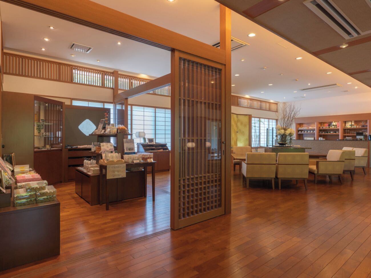 A spacious lobby with wooden flooring, a reception desk, seating area, and large windows allowing natural light.