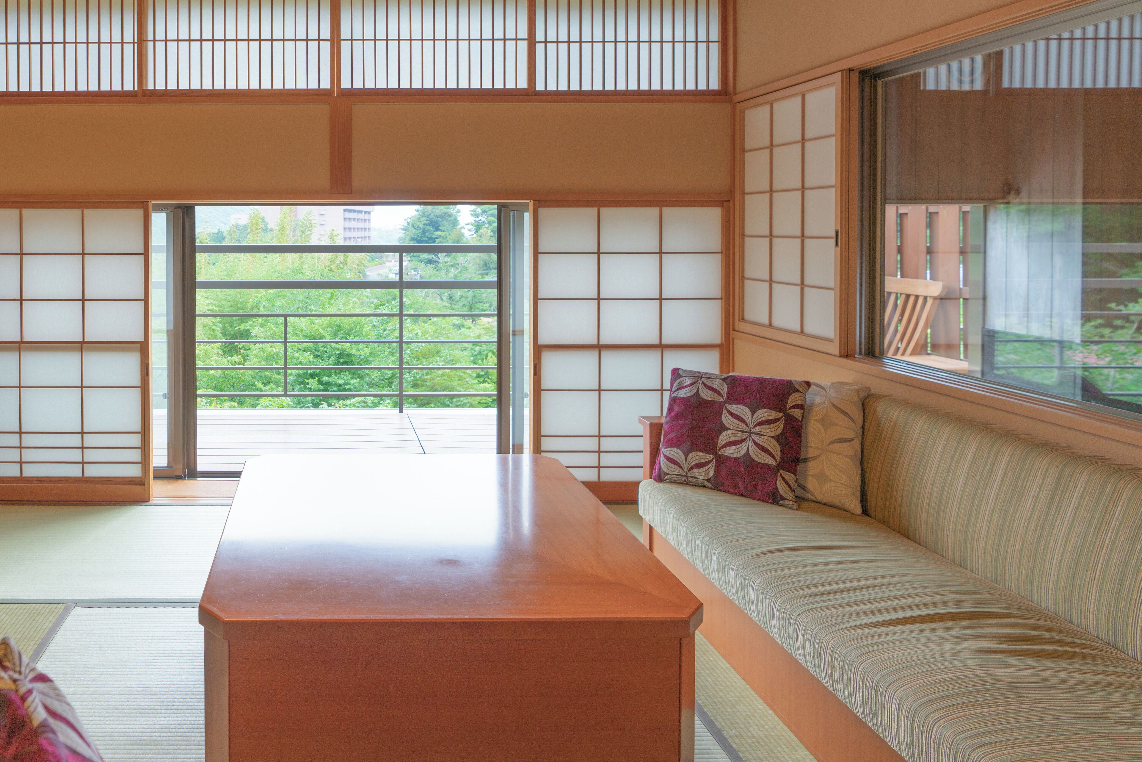 Ein traditioneller japanischer Raum mit Tatami-Böden, einem niedrigen Holztisch und einer Couch mit Kissen.
