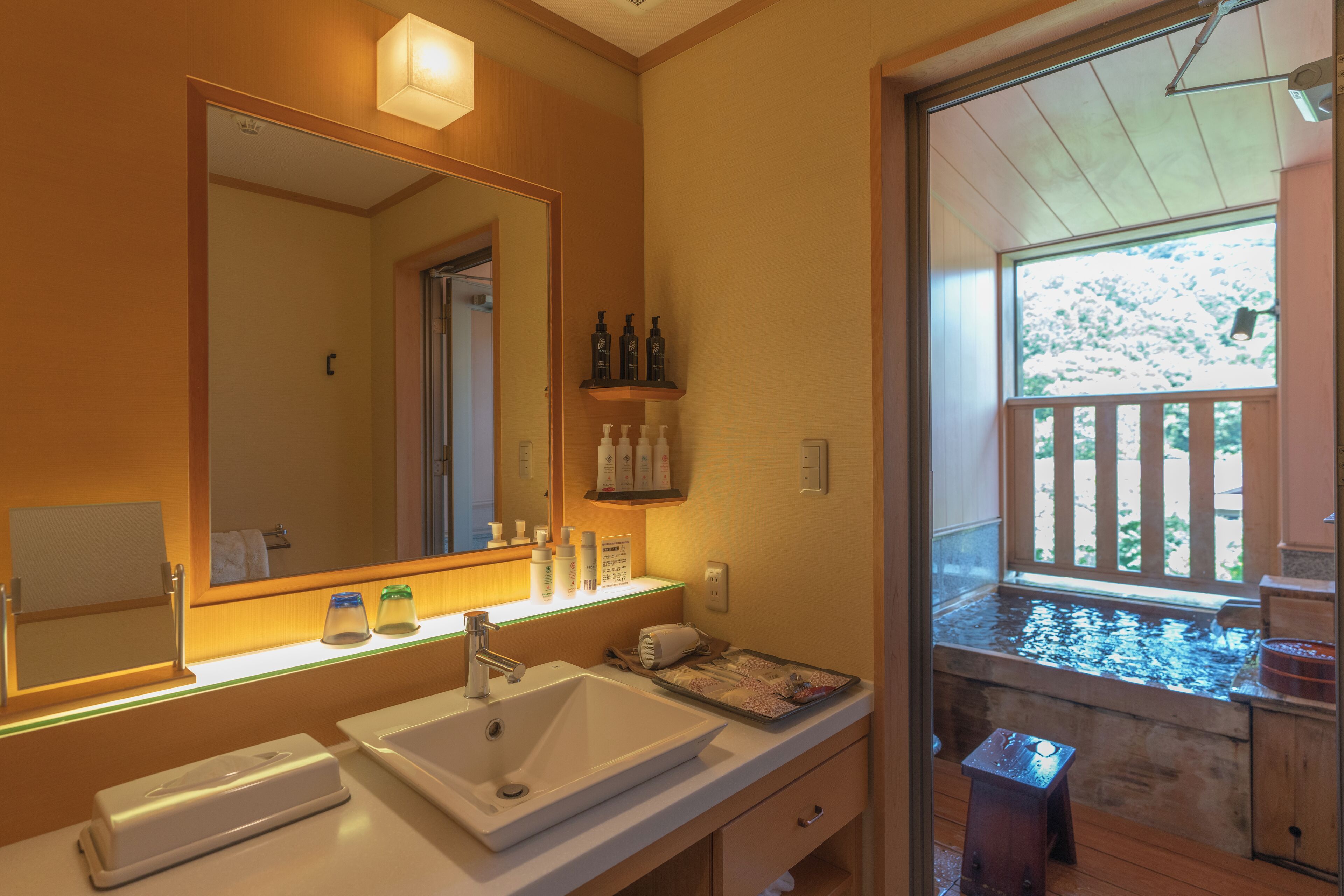Une salle de bain dotée d’un grand miroir, de deux lavabos, d’une douche et d’une fenêtre donnant sur une terrasse en bois.