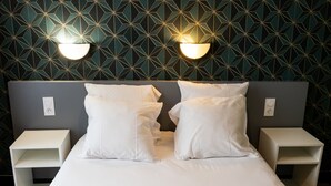 Ein Hotelzimmer mit Wandverkleidung in geometrischem Muster, einem Bett mit weißer Bettwäsche, zwei Nachttischen und Wandlampen.