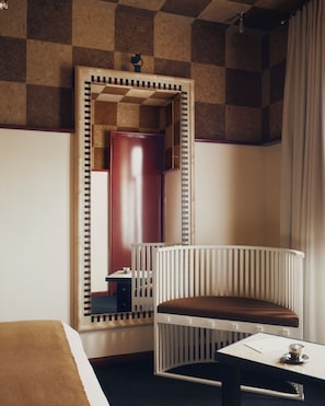 A hotel room with a checkered ceiling, a white bed, a wooden bench, a small table with a cup, and a mirror with a checkered frame. - Luxia Hotel & Spa (Paris)