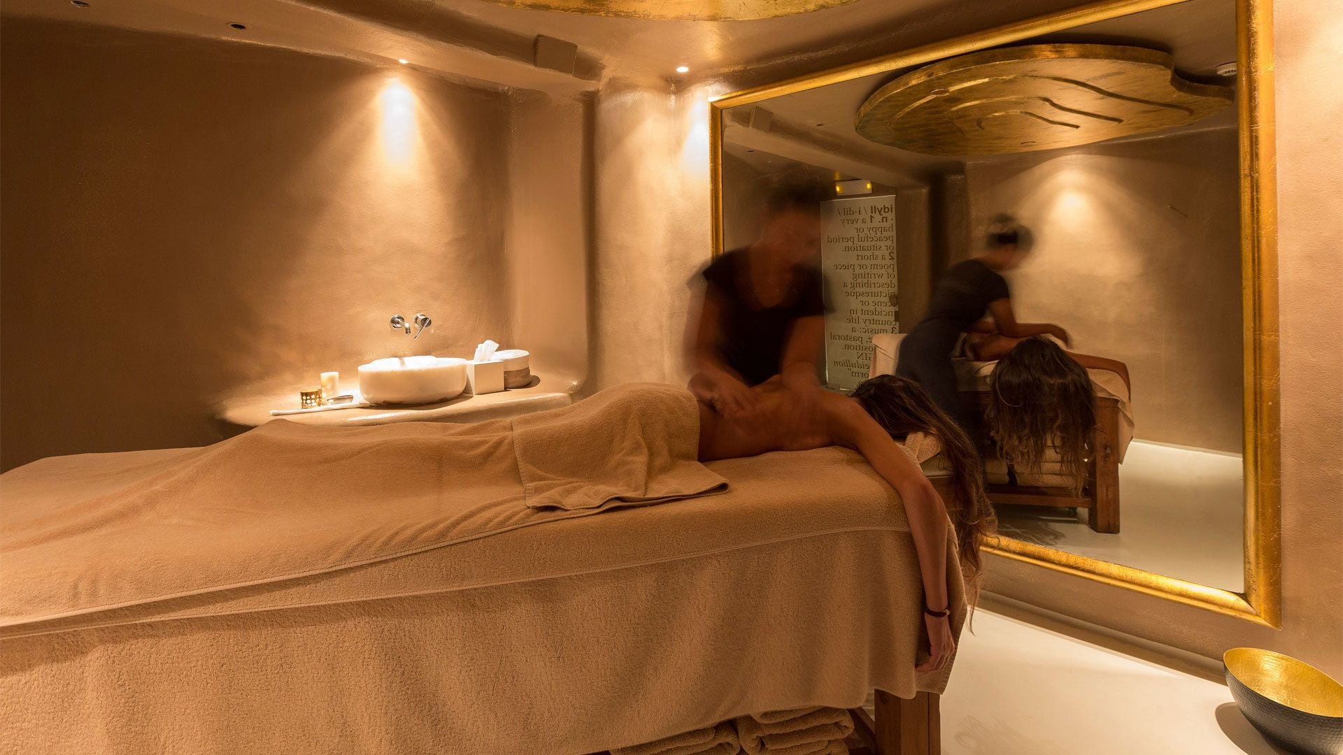 A spa room with a bed, a sink, and a large mirror.