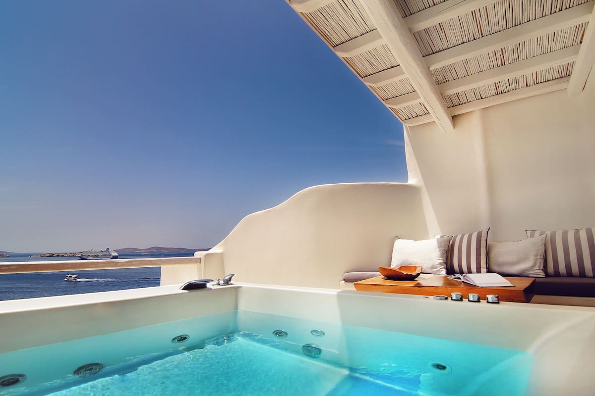A private hot tub with a view of the sea and a lounge area with a sofa and cushions.