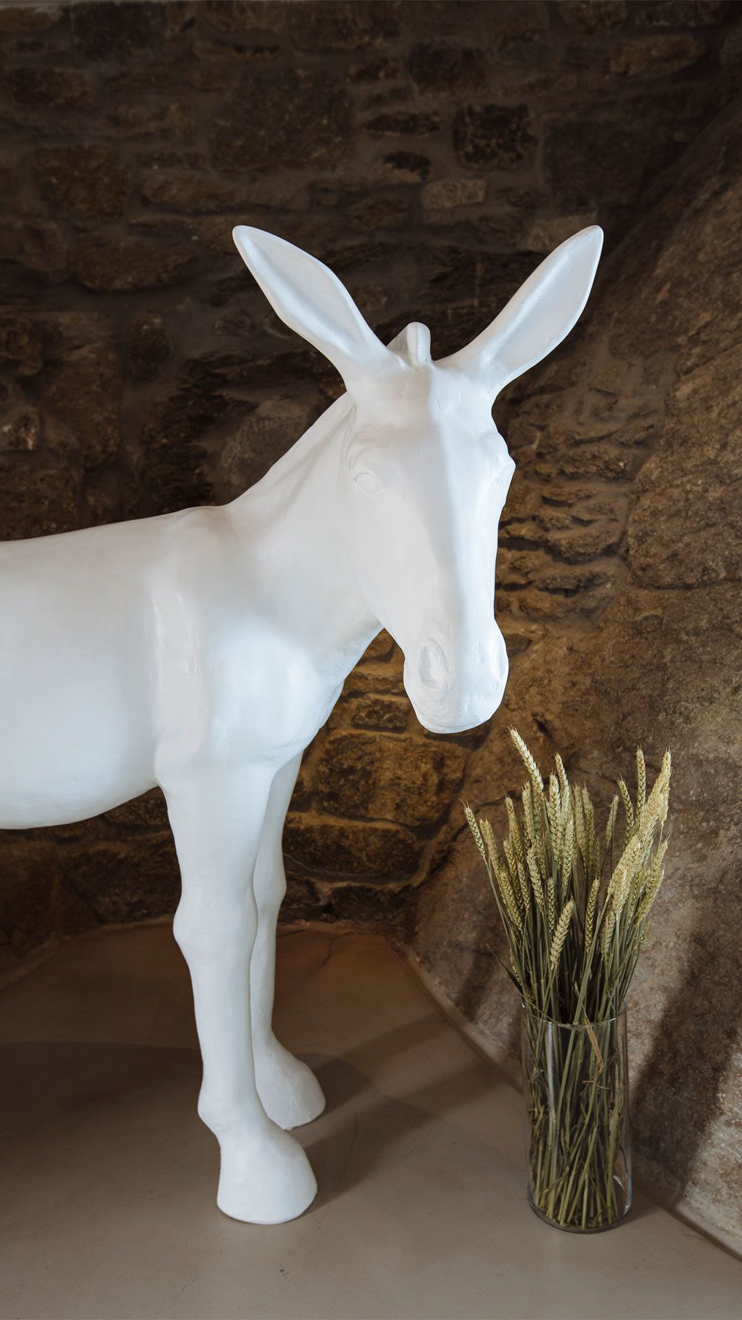 A white donkey sculpture next to a vase with wheat stalks.