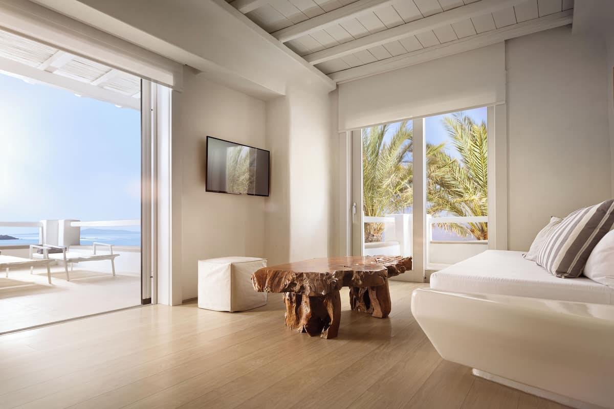 A modern living room with a wooden coffee table, white sofa, and a large window overlooking the ocean.