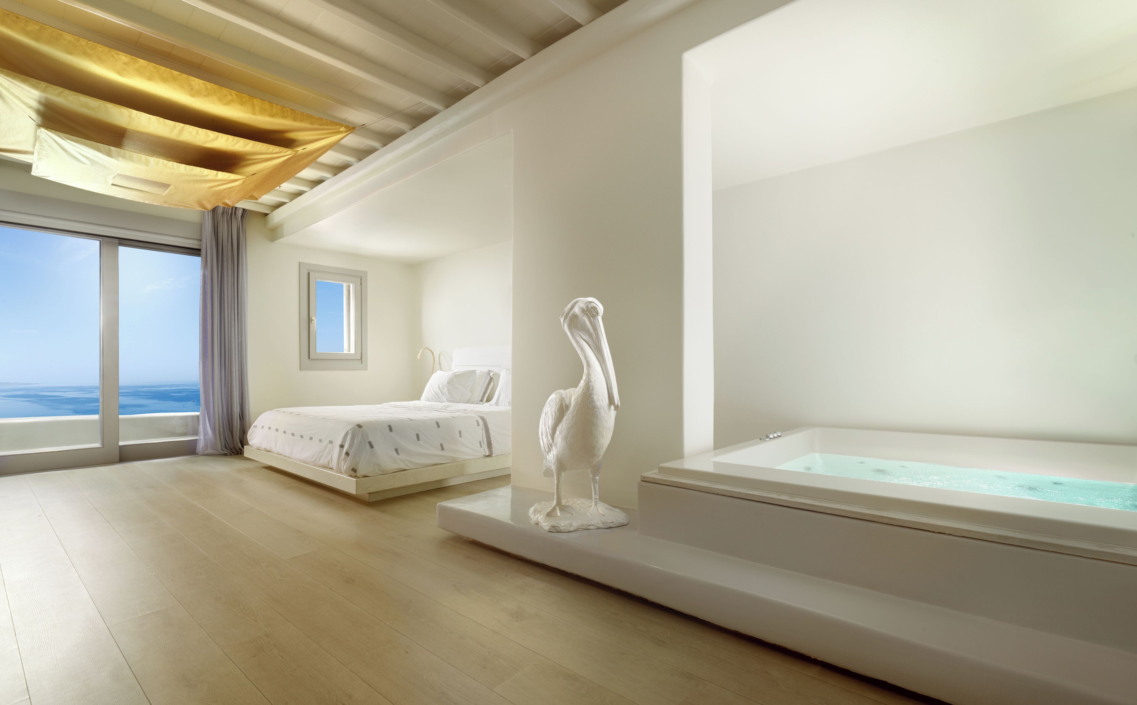 A modern bedroom with a large window, a bed, a sculpture, and a bathtub.