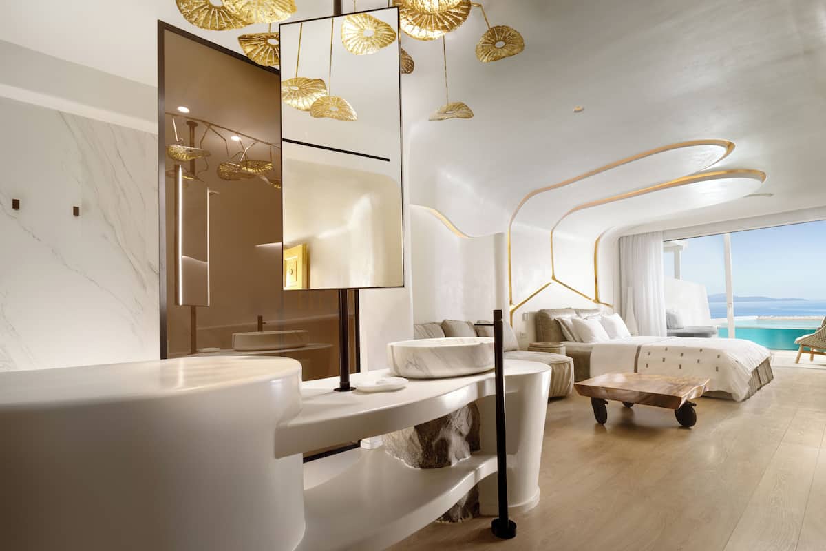 A modern hotel room with a marble bathroom, a large bed, and a view of the sea.
