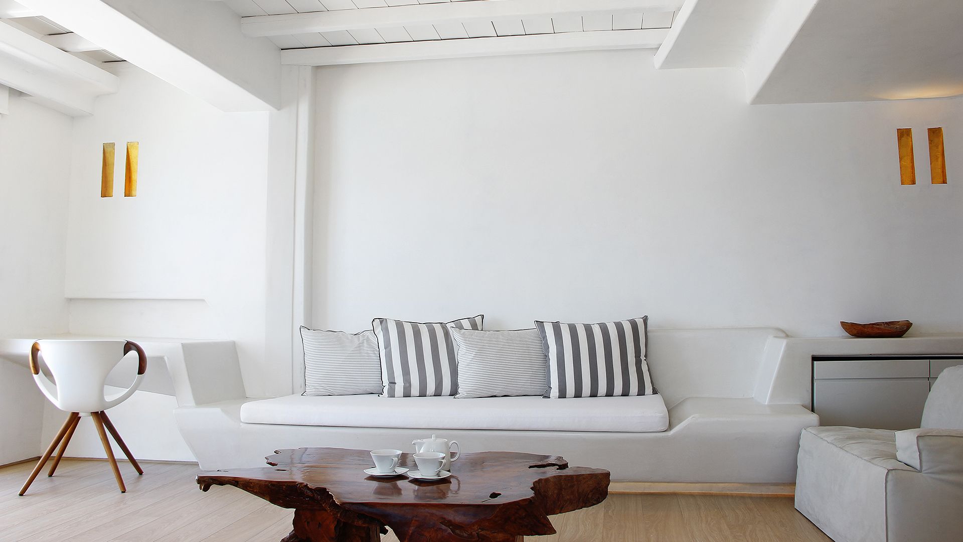 A modern living room with a white sofa, striped pillows, a wooden coffee table, and a white chair.