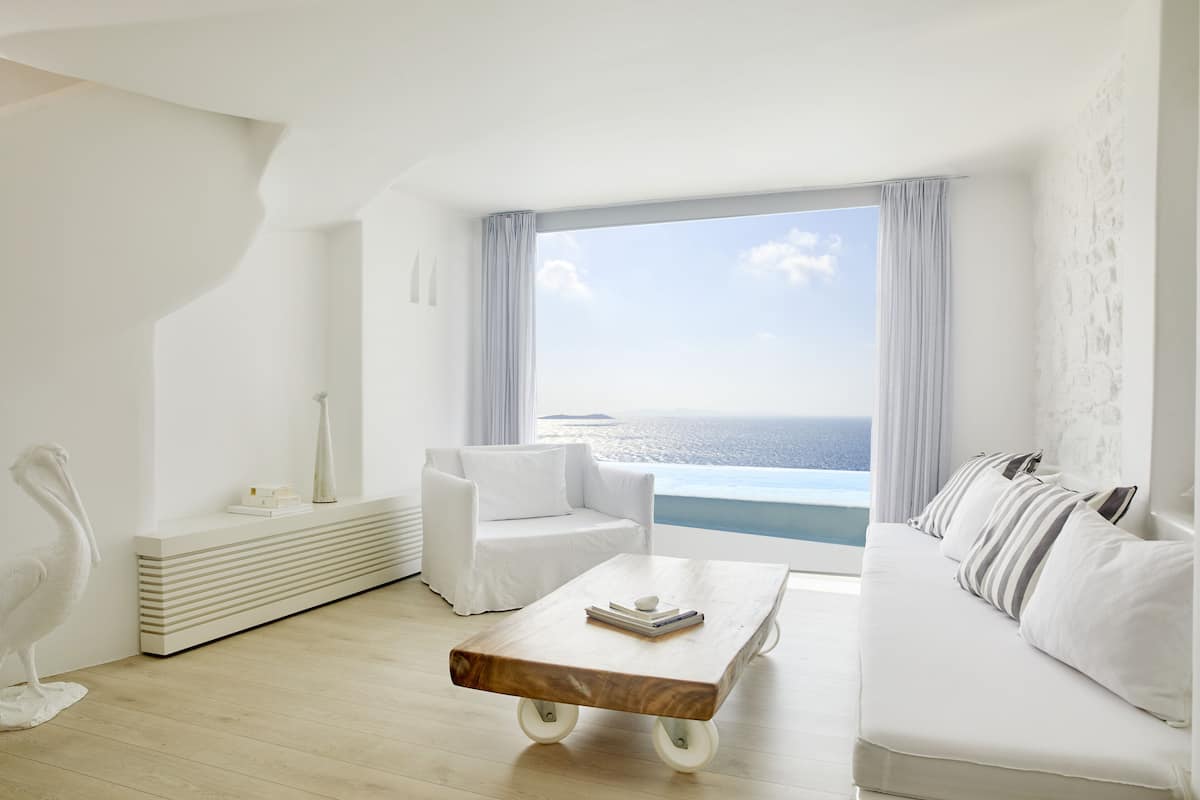A modern, minimalist living room with a view of the ocean, featuring a white sofa, a coffee table, and a white chair.