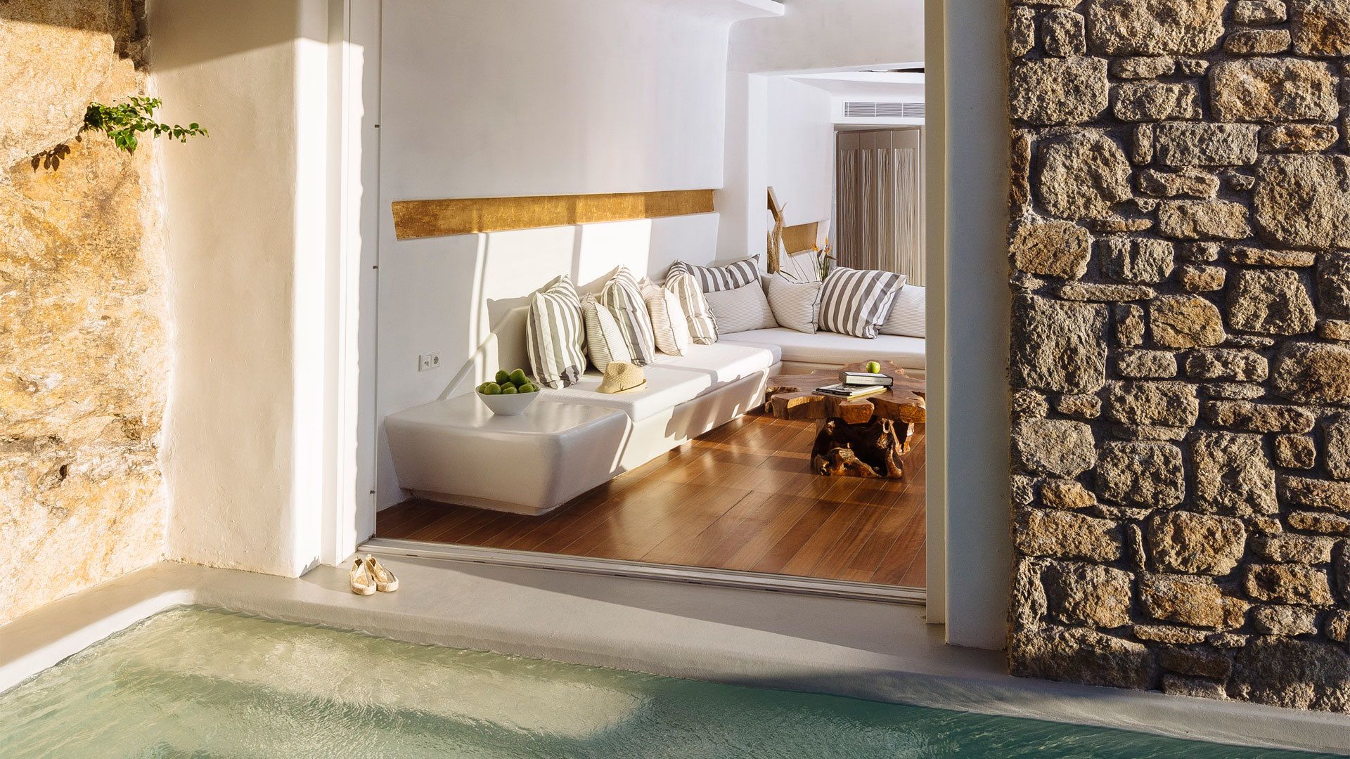 A modern living room with a stone wall, a white sofa, striped pillows, and a wooden coffee table.