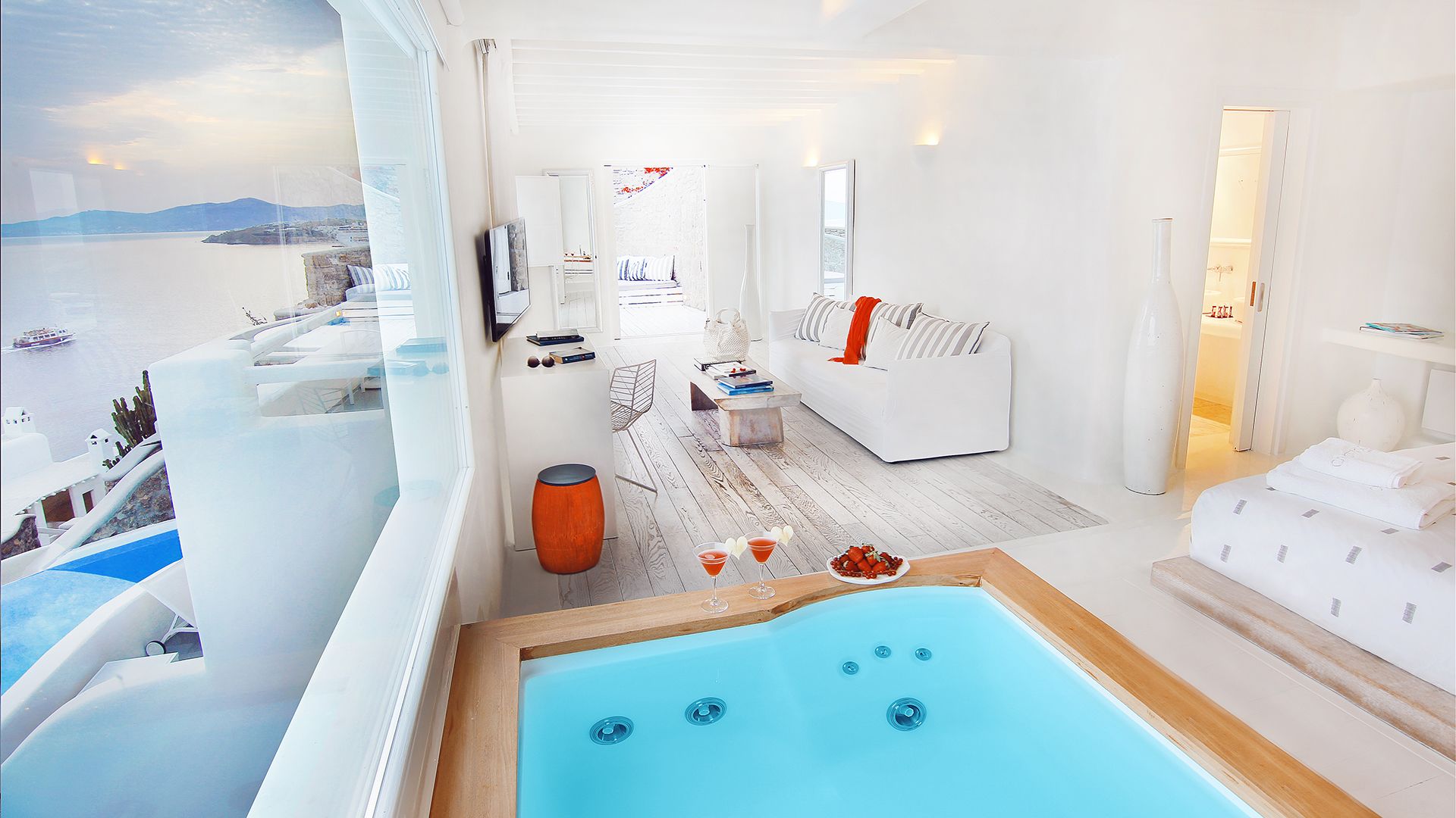 A modern, minimalist room with a large window overlooking a body of water. There is a wooden bench with a blue bathtub in the foreground.