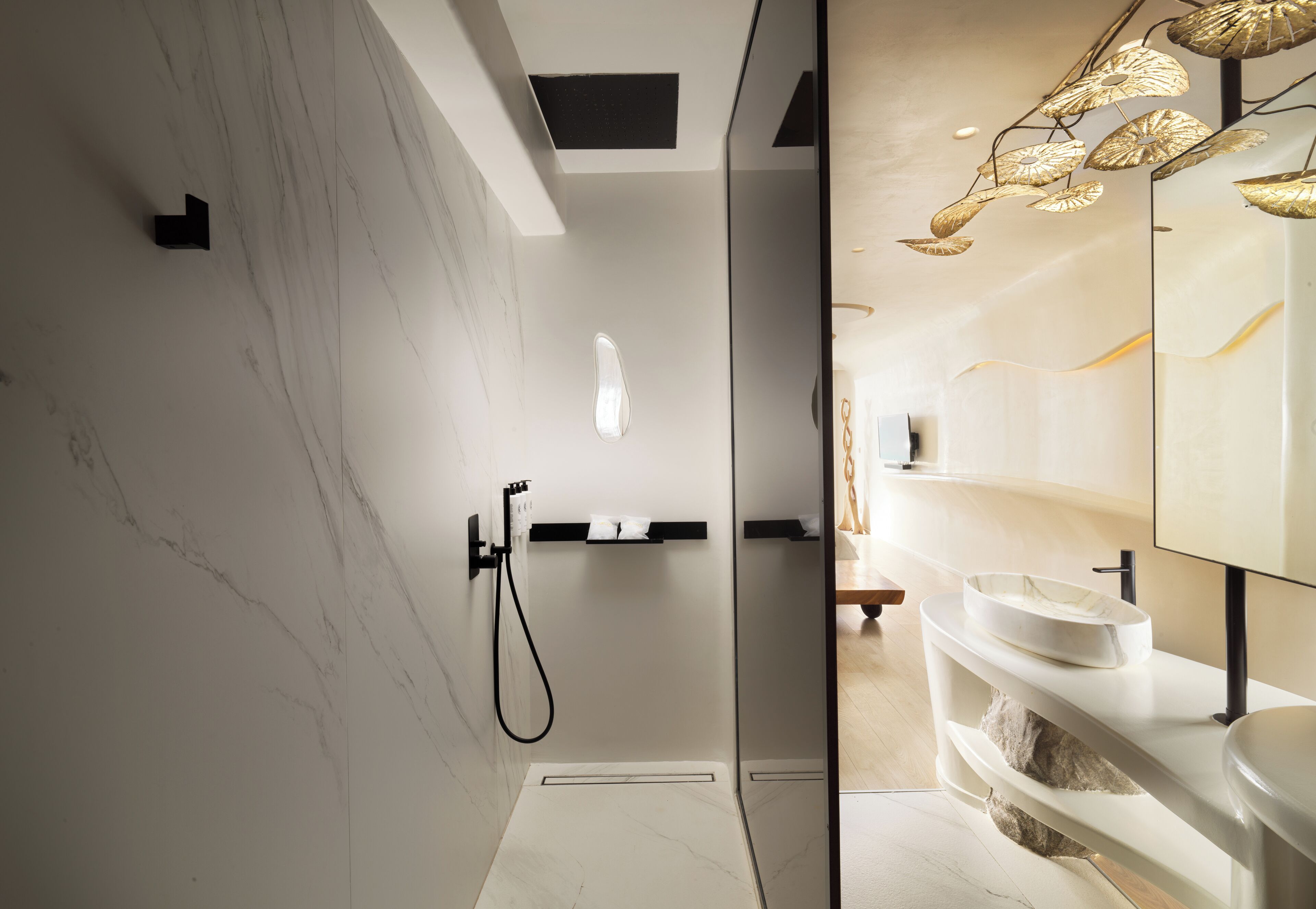 Un baño moderno con cabina de ducha de vidrio, pared de mármol blanco y tocador con espejo y lavamanos.