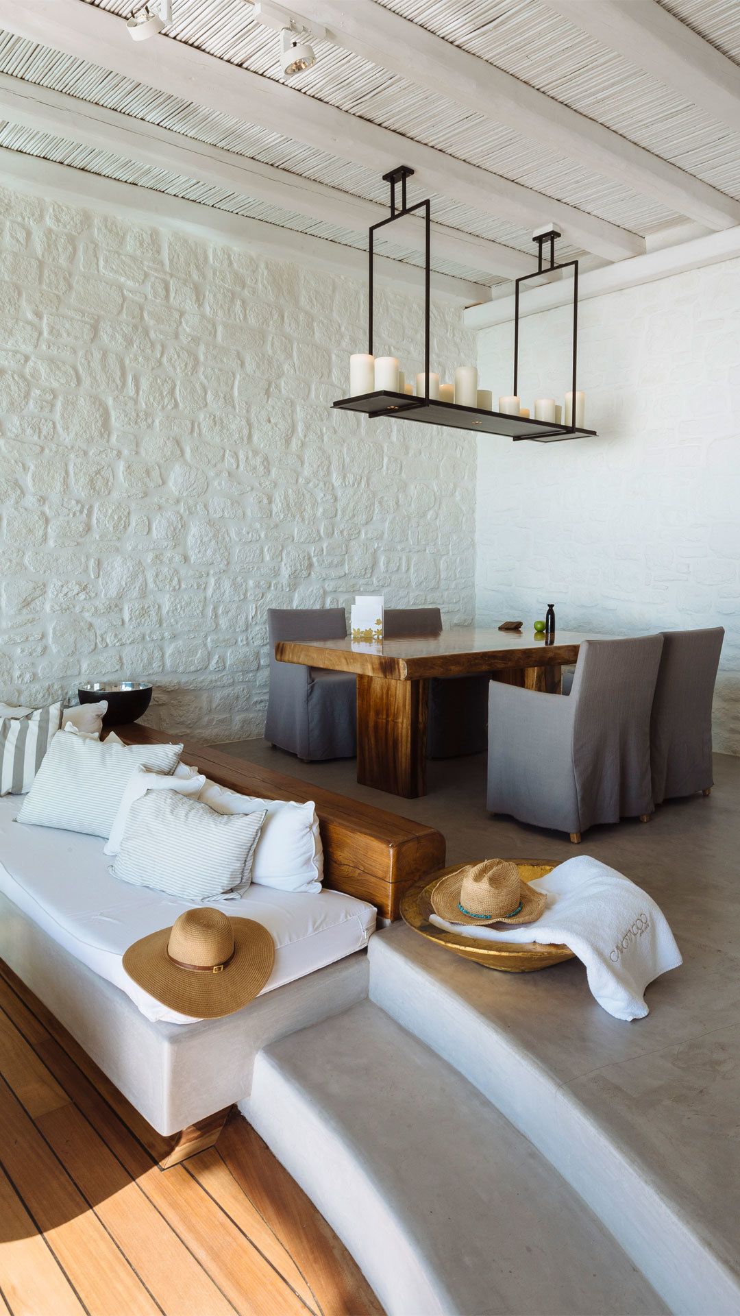 A modern living room with a stone-textured wall, a wooden dining table with grey upholstered chairs, a sofa with cushions, and a hanging light fixture.